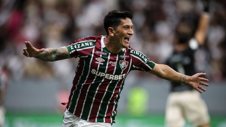 Imagem mostra Cano celebrando gol e de braços abertos com a camisa listrada com o símbolo do Fluminense